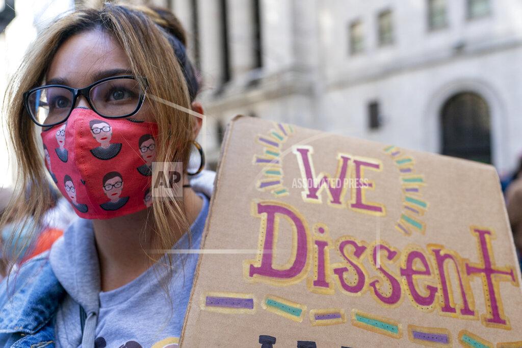 Mary Altaffer A demonstrator wears a Ruth Bader Ginsberg face mask during a Women's March rally outside the New York Stock Exchange, Saturday, Oct. 17, 2020, in New York. Dozens of Women's March rallies were planned from New York to San Francisco to signal opposition to President Donald Trump and his policies, including the push to fill the seat of late Supreme Court Justice Ruth Bader Ginsburg before Election Day. (AP Photo/Mary Altaffer)