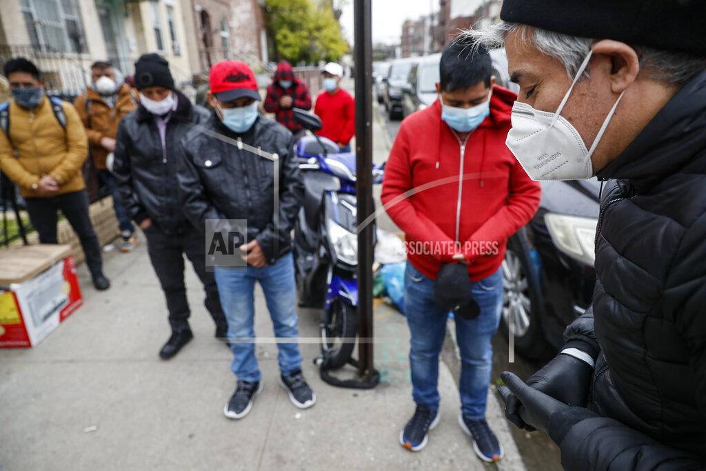 John Minchillo Fabian Arias, a Lutheran pastor with Saint Peter's Church in Manhattan, right, offers a prayer to men wearing personal protective equipment before distributing food donations on a sidewalk, Friday, May 8, 2020, in the Brooklyn borough of New York. (AP Photo/John Minchillo)