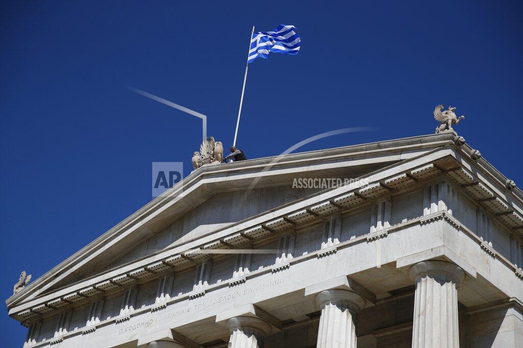 A worker adjusts the Greek flag atop of the old National Library building in Athens, Wednesday, March 17, 2021. Greece launched a 30-year government bond auction on Wednesday, hoping to take advantage of low interest rates and improve its debt profile, in part to offset the impact of the pandemic on the country's public finances. (AP Photo/Thanassis Stavrakis)