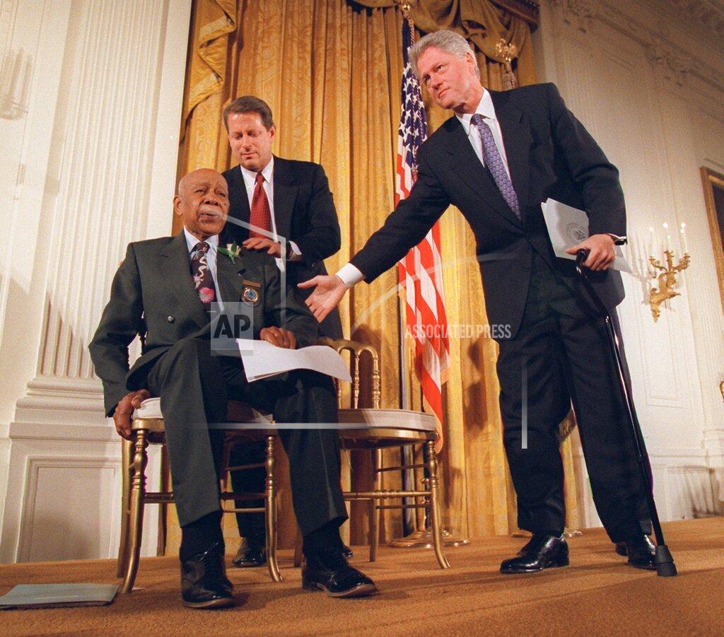Doug Mills FILE - In this May 16, 1997, file photo, President Bill Clinton and Vice President Al Gore, back, help Herman Shaw, 94, a Tuskegee Syphilis Study victim, during a news conference. Making amends for a shameful U.S. experiment, Clinton apologized to black men whose syphilis went untreated by government doctors. (AP Photo/Doug Mills, File)