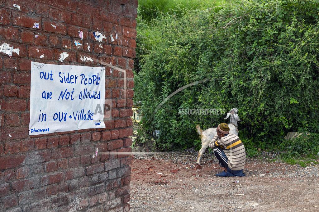 Ashwini Bhatia An elderly man sits with his goat at the entrance of Naddi village with a signboard denying entrance to outsiders stuck on a wall in Dharmsala, India, Saturday, June 12, 2021. (AP Photo/Ashwini Bhatia)