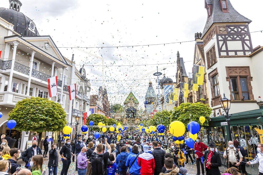 Philipp Von Ditfurth Visitors of Europa-Park walk through an avenue at the entrance of the park while employees of the park stand guard and confetti rains down from confetti cannons in Rust, Germany, Friday, May 21, 2021. Europa-Park is one of the first major theme parks in Germany to reopen its doors to visitors. The park in Rust welcomed visitors again after months of the Corona enforced break - as part of a model project approved by the state. (Philipp von Ditfurth/dpa via AP)