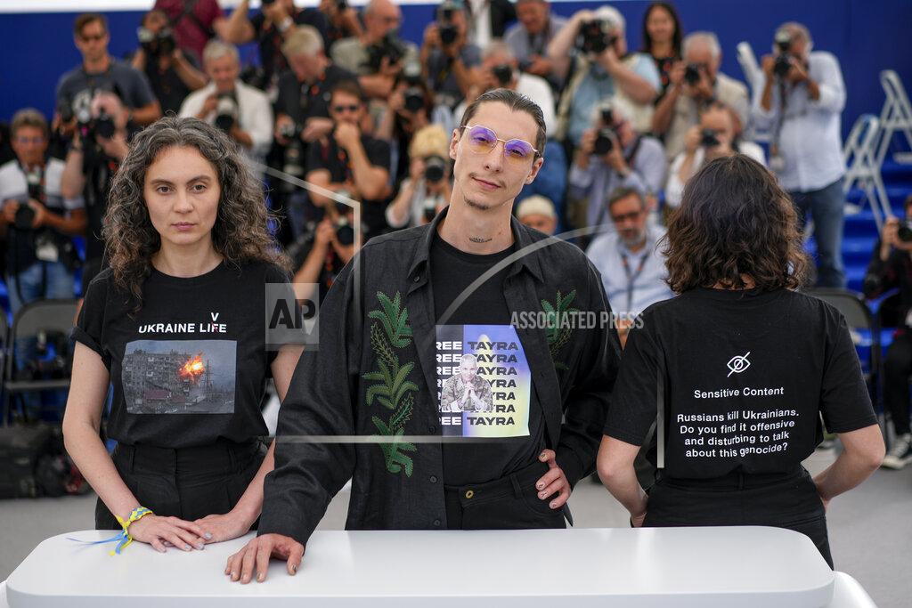 Daniel Cole Producers Darya Bassel, left, and Yelizaveta Smith, right, wearing t-shirts that have an image of an explosion on the front and read "Sensitive Content: Russians kill Ukrainians. Do you find it offensive and disturbing to talk about this genocide?" pose with director Maksym Nakonechnyi who wears a t-shirt that reads "Free Tayra" in reference to Julia Paevska, aka Tayra, a Ukrainian medic who Russian forces have taken captive at the photo call for the film 'Butterfly Vision' at the 75th international film festival, Cannes, southern France, Wednesday, May 25, 2022. (AP Photo/Daniel Cole)