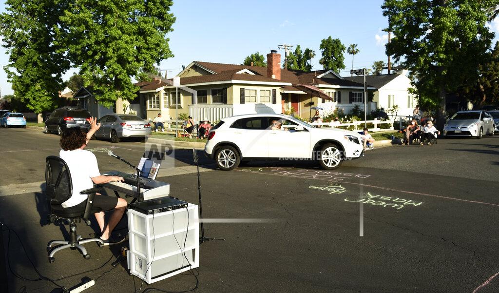 Chris Pizzello In this May 9, 2020 photo, musician Adam Chester, left, waves to a neighbor driving by as he performs his weekly neighborhood concert in the Sherman Oaks section of Los Angeles. Normally, Chester is a surrogate Elton John, who sings and plays the rock superstar's parts at rehearsals. With that work on hold, Chester has been giving concerts to his neighbors from a safe social distance in front of his house. (AP Photo/Chris Pizzello)