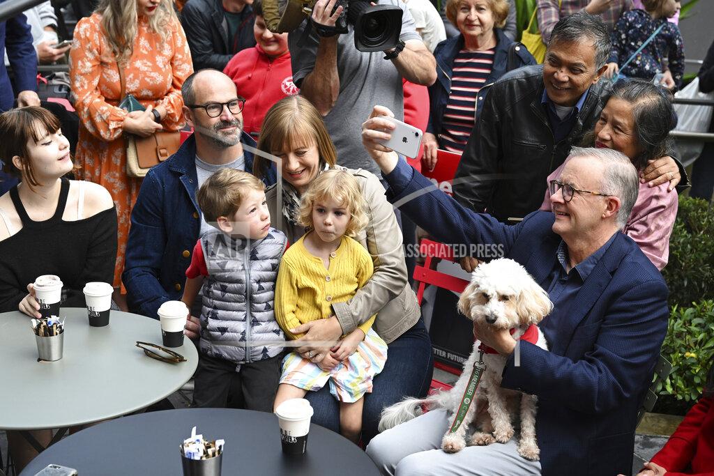 Dean Lewins Australia's Prime Minister-elect Anthony Albanese, right, with his dog Toto, on his lap, takes a photo with community members while having coffee in Sydney, Sunday, May 22, 2022. Albanese has promised to rehabilitate Australia's international reputation as a climate change laggard with steeper cuts to greenhouse gas emissions. (Dean Lewins/AAP Image via AP)
