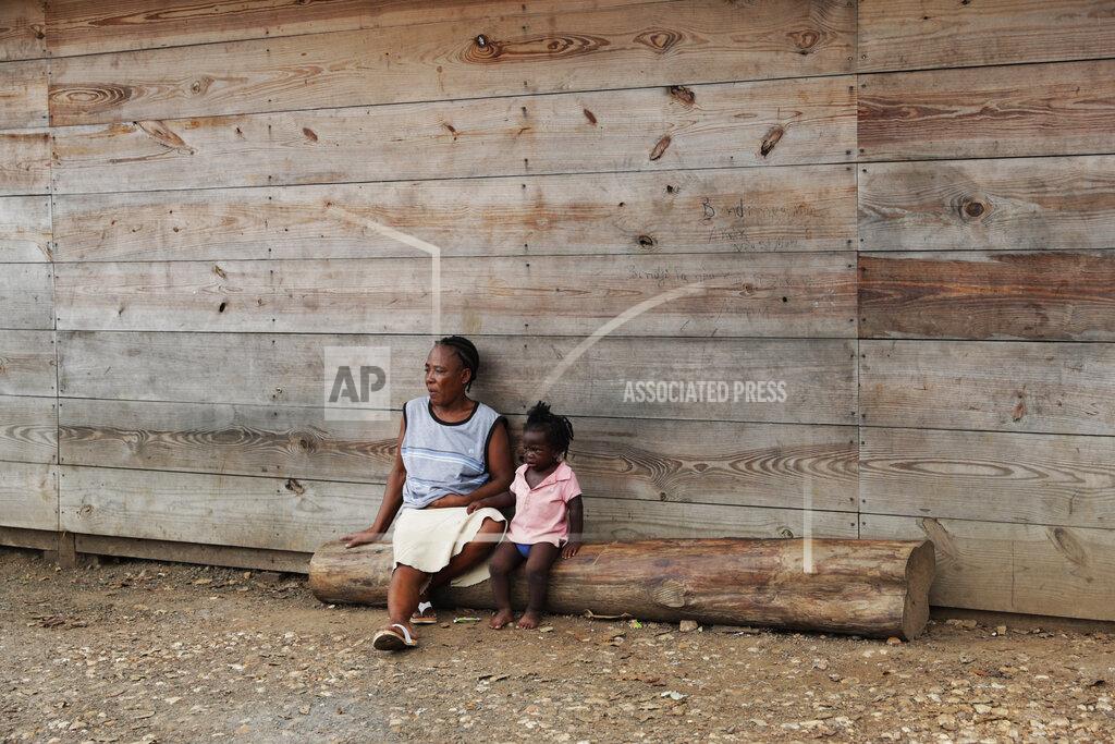 Arnulfo Franco Duperat Laurette sits on a log with a girl at the entrance of a migrant shelter in Lajas Blancas, Darien province, Panama, Saturday, Aug. 29, 2020. The 45-year-old Haitian migrant and her husband emerged from the thick jungle that blankets the Panama-Colombia border here in Darien seven months earlier and have advanced no farther because of the new coronavirus pandemic. (AP Photo/Arnulfo Franco)