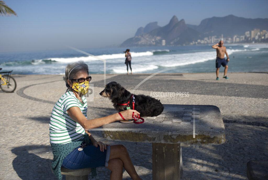 Silvia Izquierdo Lucia and her dog Jujuba sit at Arpoador beach, amid the new coronavirus pandemic in Rio de Janeiro, Brazil, Tuesday, June 2, 2020. Rio, the city with the second-most cases after Sao Paulo, is beginning to gradually relax restrictions on Tuesday, only allowing people to exercise on the beachfront sidewalk and practice individual activities in the sea. No one is allowed on the sand. (AP Photo/Silvia Izquierdo)