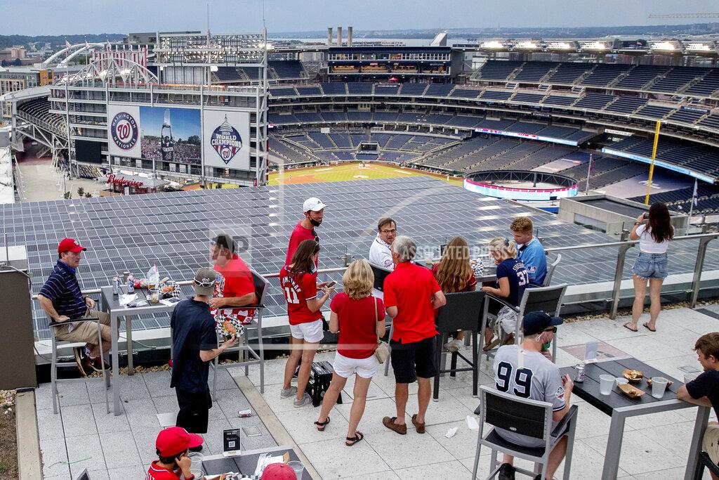 Andrew Harnik People watch the game from the Top of the Yard bar on the rooftop of Hampton Inn & Suites hotel during an opening day baseball game between the New York Yankees and the Washington Nationals at Nationals Park, Thursday, July 23, 2020, in Washington. (AP Photo/Andrew Harnik)