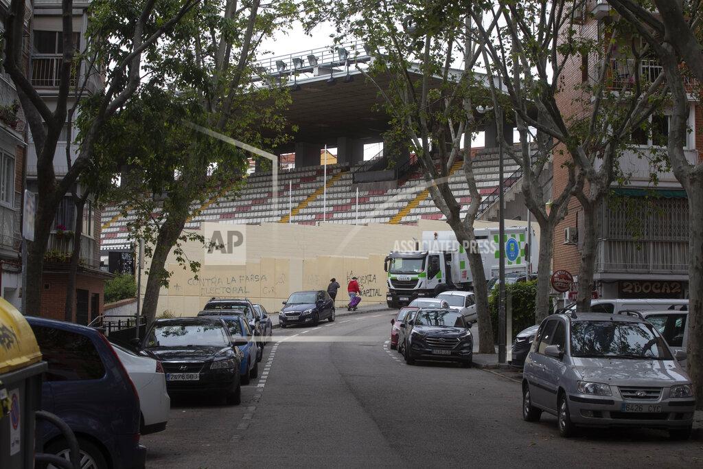 A couple walk past the closed stadium of Spanish 2nd division club Rayo Vallecano in Madrid, Spain, Thursday May 14, 2020. Soccer players in Spain are currently allowed to undergo individual training sessions at their team's training camps, with longer group sessions and full squad practices expected in the coming weeks if the coronavirus pandemic doesn't get worse. La Liga president Javier Tebas has said he hopes the league can restart on June 12. (AP Photo/Paul White)