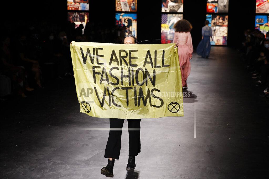 An activist displays a banner during Dior's Spring-Summer 2021 fashion collection presented Tuesday, Sept. 29, 2020 during the Paris fashion week. (AP Photo/Francois Mori)