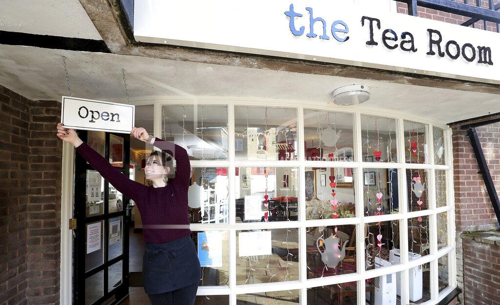 Harriet Henry, manager of The Tea Room in Knutsford, England, poses with the Open sign outside her cafe, as she prepares to open, Sunday April 11, 2021. Millions of people in Britain will get their first chance in months for haircuts, casual shopping and restaurant meals on Monday, as the government takes the next step on its lockdown-lifting roadmap. (Martin Rickett/PA via AP)