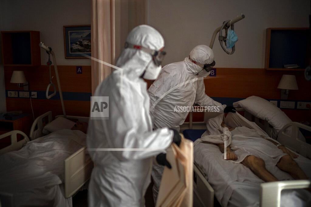 Emilio Morenatti Separated by a curtain, a person sleeps in a bed as mortuary workers prepare the body of an elderly person who died of COVID-19 before removing it from a nursing home in Barcelona, Spain, Thursday, Nov. 19, 2020. Virus cases among the elderly are again on the rise across Europe, causing havoc and rising death tolls in nursing homes despite the lessons of a tragic spring. Authorities are in a race to save lives as they wait for crucial announcements on mass vaccinations. (AP Photo/Emilio Morenatti)