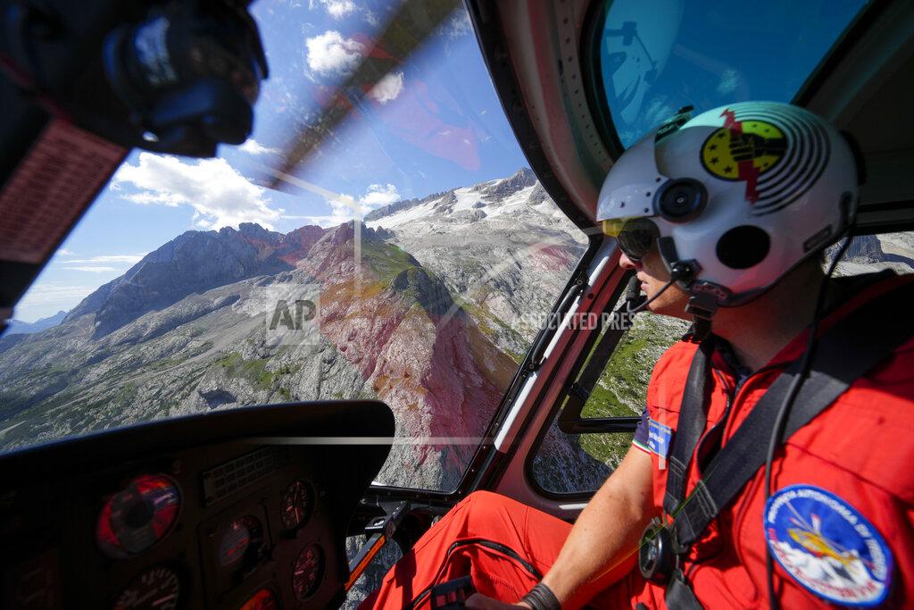 Luca Bruno A rescuer pilots a helicopter to conduct searches for the victims of the Punta Rocca glacier avalanche in Canazei, in the Italian Alps in northern Italy, Tuesday, July 5, 2022, two days after a huge chunk of the glacier broke loose, sending an avalanche of ice, snow, and rocks onto hikers. Italy was enduring a prolonged heat wave before a massive piece of the Alpine glacier broke off and killed hikers on Sunday and experts say climate change will make those hot, destabilizing conditions more common. (AP Photo/Luca Bruno)
