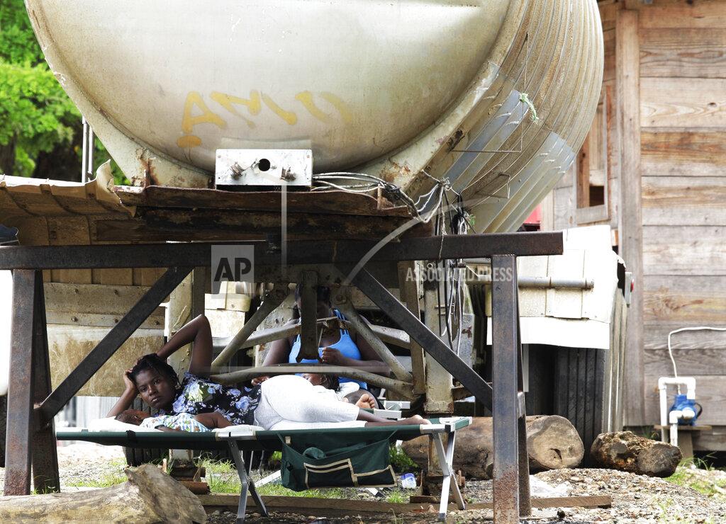 Arnulfo Franco Women and children rest under a water tank at a migrant camp in Lajas Blancas, Darien province, Panama, Saturday, Aug. 29, 2020. The flow of migrants through the dense and dangerous Darien jungle has been going strong for more than a decade. This is the first time authorities have stopped it because of the ongoing new coronavirus pandemic. (AP Photo/Arnulfo Franco)