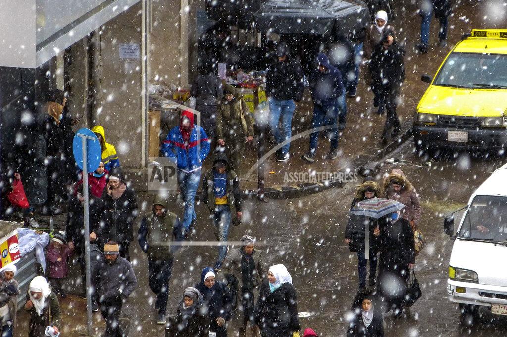 Uncredited In this photo released by the Syrian official news agency SANA, people walk on a street as snow falls, in Damascus, Syria, Wednesday, Feb. 17, 2021. Snow blanketed parts of Syria, Lebanon, Jordan and Israel on Wednesday, blocking roads, disrupting traffic and postponing vaccination campaigns against COVID-19 and even exams at some universities. (SANA via AP)