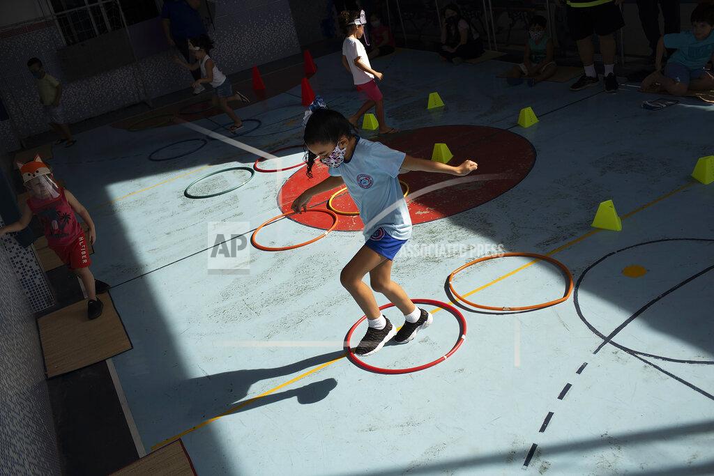 Silvia Izquierdo Rafaely de Melo, wearing a protective mask, jumps during gym class at the Pereira Agustinho daycare, nursery school and pre-school, after it reopened amid the new coronavirus pandemic in Duque de Caxias, Monday, July 6, 2020. The city of Manaus in the Amazon rainforest and Duque de Caxias in Rio de Janeiro’s metropolitan region, became on Monday the first Brazilian cities to resume in-person classes at private schools since the onset of the COVID-19 pandemic, according to the nation's private school federation. (AP Photo/Silvia Izquierdo)