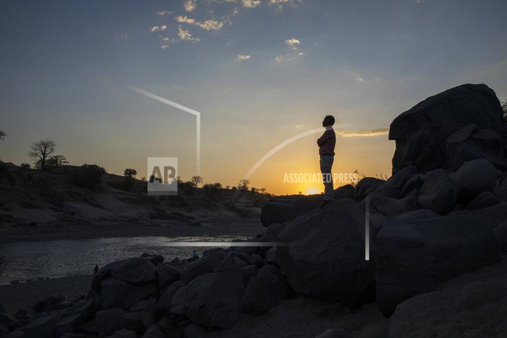 Nariman El-Mofty Surgeon and doctor-turned-refugee, Dr. Tewodros Tefera, stands at the Tezeke River crossing in Hamdayet, Sudan, on March 16, 2021. At left across the river is Ethiopia. He plans to continue his work in Sudan. The high-rise buildings of his city in Tigray, Humera, can be seen on the horizon. He could walk home, but he’s not sure he will ever go there again. (AP Photo/Nariman El-Mofty)