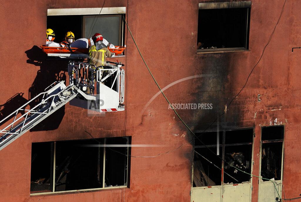 Joan Mateu Firefighters load the body of a dead person into a crane after a fire on a building in Badalona, Barcelona, Spain, Thursday, Dec. 10, 2020. Authorities in northeastern Spain say a fire has raged through an abandoned building occupied by squatters in the city of Badalona, injuring at least 17 people, including two in critical condition. Firefighters say they rescued around 30 people from windows as the building burned late Wednesday. (AP Photo/Joan Mateu)