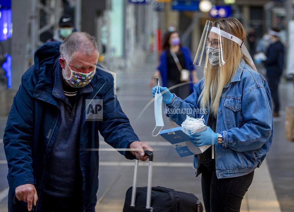 Michael Probst FILE - In this April 27, 2020 file photo, a woman working for the regional public transport company offers a face mask to an elderly man in the main train station in Frankfurt, Germany. More than 50,000 people have died after contracting COVID-19 in Germany, a number that has risen swiftly over recent weeks as the country has struggled to bring down infection figures. (AP Photo/Michael Probst, File)