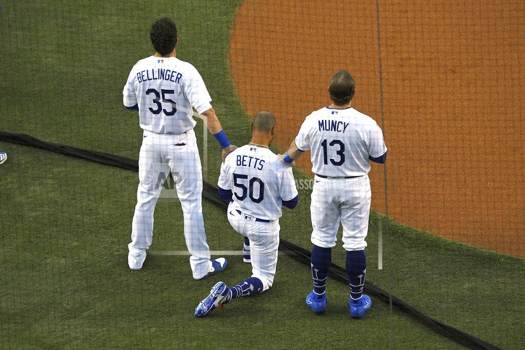Los Angeles Dodgers' Cody Bellinger, left, and Max Muncy, right, put their hands on Mookie Betts during the national anthem prior to an opening day baseball game Thursday, July 23, 2020, in Los Angeles. (AP Photo/Mark J. Terrill)
