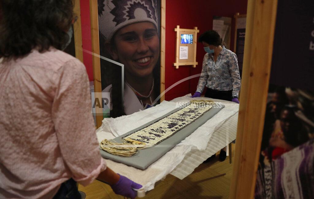 Alastair Grant Co-curator Jo Loosemore, right, and Kate Johnson, Exhibitions Office Plymouth, move a recently created wampum belt made by members of the Wampanoag Native America people, after its unpacking and prior to it going on display in Southampton, England, Thursday, Aug. 13, 2020. On the 400th anniversary of the Mayflower voyage, commemorations are focusing on both the Pilgrim settlers and the Native people whose lives were transformed by their arrival. An exhibition in England focuses on one casualty of colonization: a wampum belt taken from the Wampanoag people to England in the 17th century, and then lost. (AP Photo/Alastair Grant)