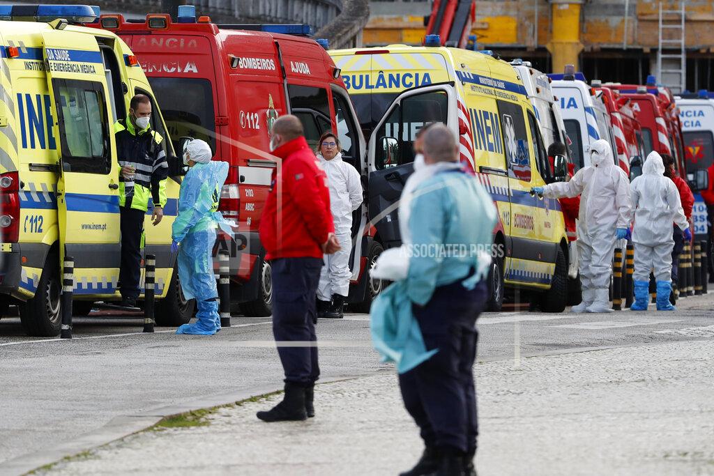 Ambulance personnel stand waiting as more than a dozen ambulances queue waiting to hand over their COVID-19 patients to medics at the Santa Maria hospital in Lisbon, Friday, Jan. 22, 2021. Portugal's COVID-19 surge is continuing unabated, with a new record of daily deaths, hospitalizations and patients in intensive care. (AP Photo/Armando Franca)