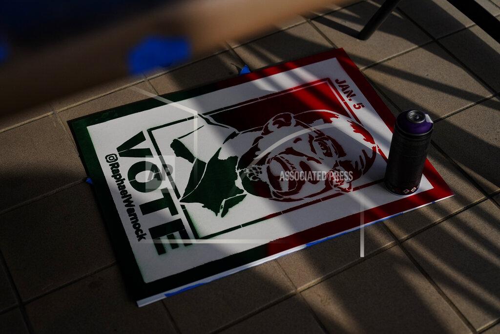 Brynn Anderson A campaign poster sits on the ground near where artist Brandon Litman, 39, of Brooklyn, N.Y., spray paints more posters after Georgia's Senate runoff race on Saturday, Jan. 9, 2021, in Atlanta. (AP Photo/Brynn Anderson)