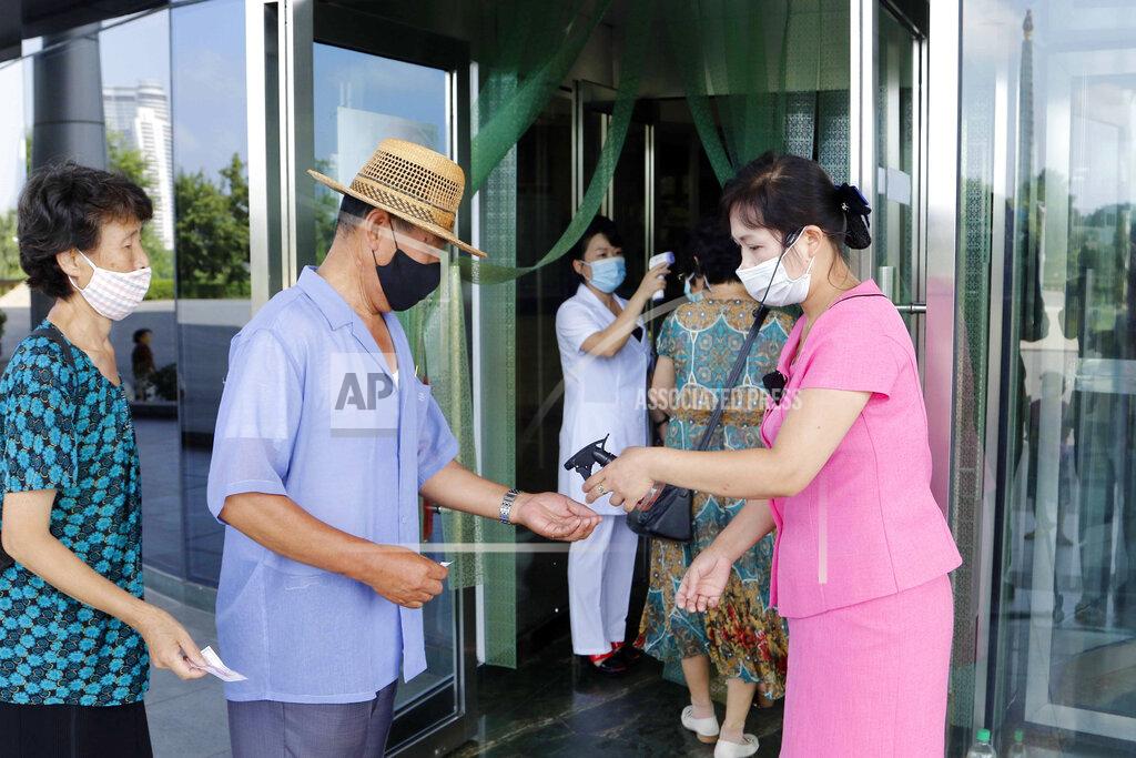 Two employees of the Ryugyong Health Complex disinfect the hands and check the fever of people coming to the complex to help curb the spread of the coronavirus, in Pyongyang, North Korea, Friday, July 31, 2020. (AP Photo/Jon Chol Jin)