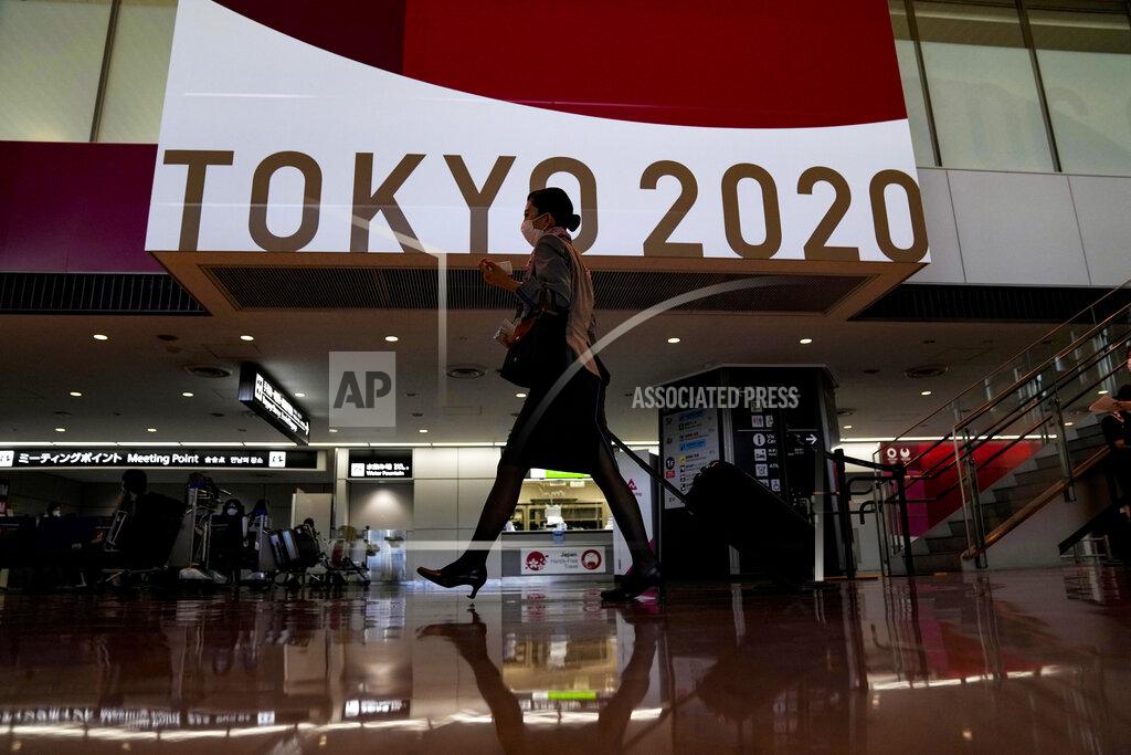 FILE - In this July 15, 2021, file photo, a flight attendant walks by a large display of Tokyo 2020 Olympics at Narita International Airport in Narita, east of Tokyo. (AP Photo/Kiichiro Sato, File)