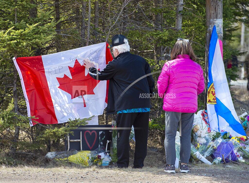 Andrew Vaughan In this Wednesday, April 22, 2020, photo, a couple place a flag at a memorial in Portapique, Nova Scotia, following Saturday's shooting rampage. (Andrew Vaughan/The Canadian Press via AP)