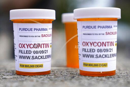 FILE - In this Aug. 9, 2021, file photo, fake pill bottles with messages about OxyContin maker Purdue Pharma are displayed during a protest outside the courthouse where the bankruptcy of the company is taking place in White Plains, N.Y. A federal judge on Wednesday, Oct. 13 allowed Purdue Pharma to resume its work carrying out the recent $10 billion settlement plan that allowed the Oxycontin maker to emerge from bankruptcy. (AP Photo/Seth Wenig, File)