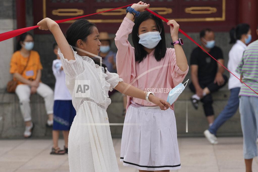 Ng Han Guan Children with masks lift up a barrier in Beijing Tuesday, Aug. 3, 2021. The coronavirus’s delta variant is challenging China’s costly strategy of isolating cities, prompting warnings that Chinese leaders who were confident they could keep the virus out of the country need a less disruptive approach. (AP Photo/Ng Han Guan)