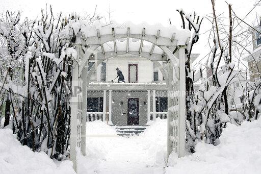 FILE - Amber Cox shovels snow from the porch roof at her home in Auburn, Maine, on March 8, 2018. With prices surging worldwide for heating oil, natural gas and other fuels, the U.S. government said Wednesday, Oct. 13, 2021 it expects households to see jumps of up to 54% for their heating bills compared to last winter. (Daryn Slover/Sun Journal via AP)