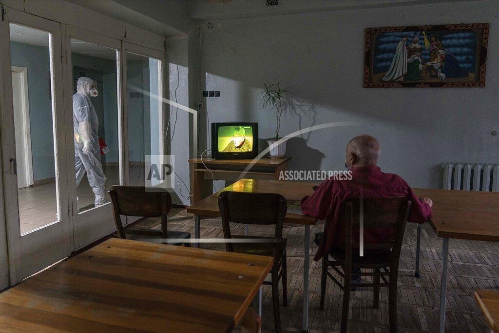 Evgeniy Maloletka A medical worker walks past a room as a coronavirus patient watches TV at a hospital in Stebnyk, Ukraine, on Tuesday, Sept. 29, 2020. As coronavirus cases increase, every bed in the hospital in this city in western Ukraine is in use and its chief doctor is watching the surge with alarm and anguish. (AP Photo/Evgeniy Maloletka)