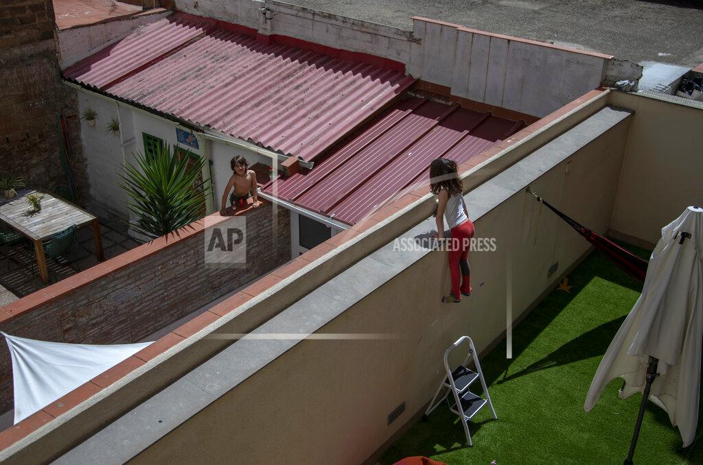 Gala, 7, speaks with her friend and classmate Oliver, 6, as they jump on the wall on their courtyard in Barcelona, Spain, Wednesday, April 29, 2020 as the lockdown to combat the spread of coronavirus continues. (AP Photo/Emilio Morenatti)