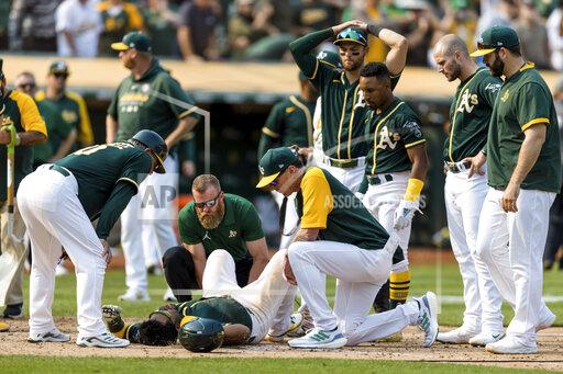 Oakland Athletics manager Bob Melvin, center right, and others attend to Elvis Andrus, center, after he collapsed with an injury after scoring a walk-off win against the Houston Astros in the ninth inning of a baseball game in Oakland, Calif., Saturday, Sept. 25, 2021. The Athletics won 2-1. (AP Photo/John Hefti)