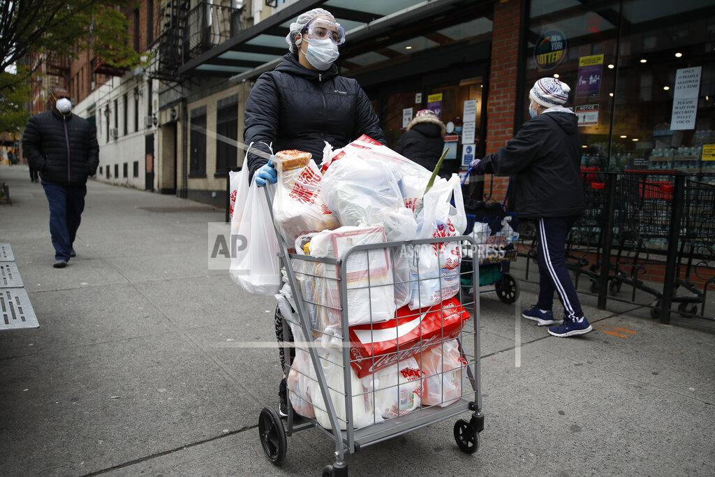 John Minchillo A shopper wears a face mask and gloves as she leaves a grocery store with a loaded cart Saturday, April 18, 2020, in the Harlem neighborhood of the Manhattan borough of New York during the coronavirus outbreak. (AP Photo/John Minchillo)