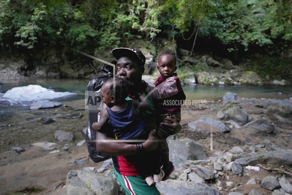 Fernando Vergara A migrant carries two children across a river as they continue their trek north, near Acandi, Colombia, Wednesday, Sept. 15, 2021. The migrants, mostly Haitians, are on their way to crossing the Darien Gap from Colombia into Panama dreaming of reaching the U.S. (AP Photo/Fernando Vergara)