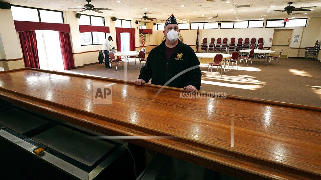 Charles Krupa With chairs stacked against the wall of their hall space, Craig DeOld, commander at Veterans of Foreign War Post #1018, poses at the empty bar rail at the post's rental space, Monday, March 15, 2021, in Boston. Local bars and halls run by the VFW and American Legion posts have fallen on hard times during the coronavirus pandemic. Organizers say many risk permanent closure after states ordered them, like other bars and halls, to shutter last spring. (AP Photo/Charles Krupa)