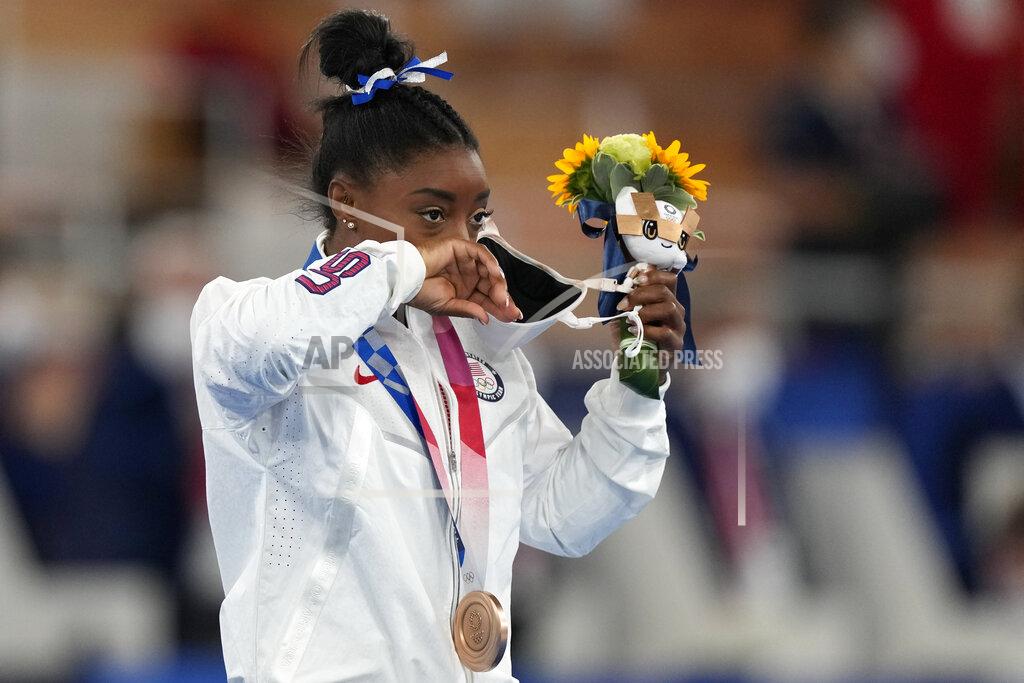 Simone Biles, of the United States, removes her face mask on the podium after winning the bronze medal on the balance beam during the artistic gymnastics women's apparatus final at the 2020 Summer Olympics, Tuesday, Aug. 3, 2021, in Tokyo, Japan. (AP Photo/Natacha Pisarenko)