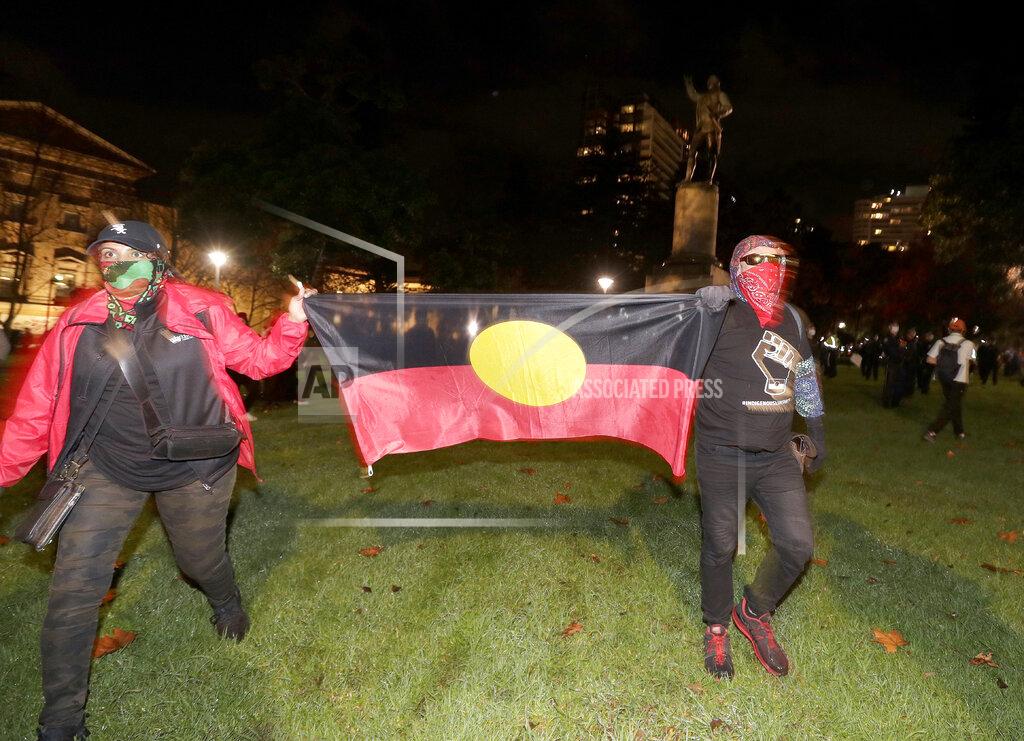 Rick Rycroft Protestoers carry an Aboriginal flag as the walk past a statue of British explorer James Cook in Sydney, Friday, June 12, 2020, to support U.S. protests over the death of George Floyd. Hundreds of police disrupted plans for a Black Lives Matter rally but protest organizers have vowed that other rallies will continue around Australia over the weekend despite warnings of the pandemic risk. (AP Photo/Rick Rycroft)
