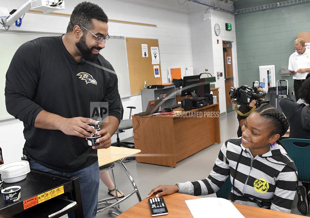 FILE - Baltimore Ravens lineman and math scholar John Urschel, left, hands out ice cream to Chelsy Valerio, 14, of Baltimore, during a lesson at Dundalk High School during the launch of Texas Instruments' STEM Behind Cool Careers series in Baltimore, in this Tuesday, July 18, 2017, file photo. John Urschel has found that a master's degree in mathematics, his stature as an accomplished author and his pending PhD at MIT isn't necessarily enough to sell young students on the benefit of crunching numbers. What really makes him interesting to most kids is that he's a former NFL player who opted to immerse himself in math. (Steve Ruark/AP Images for Texas Instruments, File)