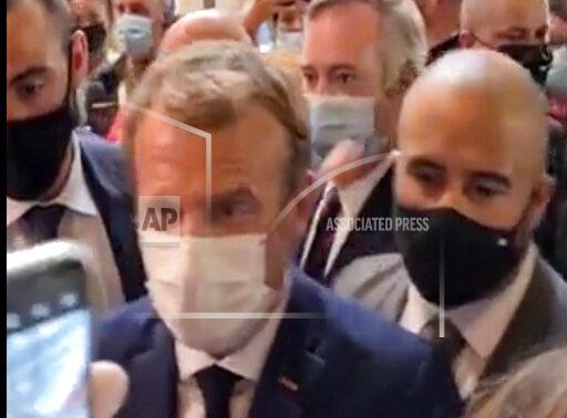 This image from video made available by Lyonmag.com shows an egg thrown toward French President Emmanuel Macron, left, to hit him on the shoulder as he walks through the restaurant trade fair in Lyon, France, Monday Sept. 27, 2021. Macron was visiting the International Catering, Hotel and Food Trade Fair to promote French gastronomy. (LYONMAG.COM via AP)