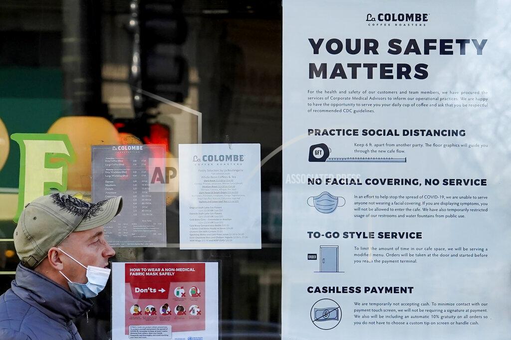Nam Y. Huh FILE - In this Nov. 12, 2020, file photo, a man walks past a coffee shop as the store displays information signs in Chicago. With the coronavirus coming back with a vengeance across the country and the U.S. facing a long, dark winter, governors and other elected officials are showing little appetite for reimposing the kind of lockdowns and large-scale business closings seen last spring. (AP Photo/Nam Y. Huh, File)