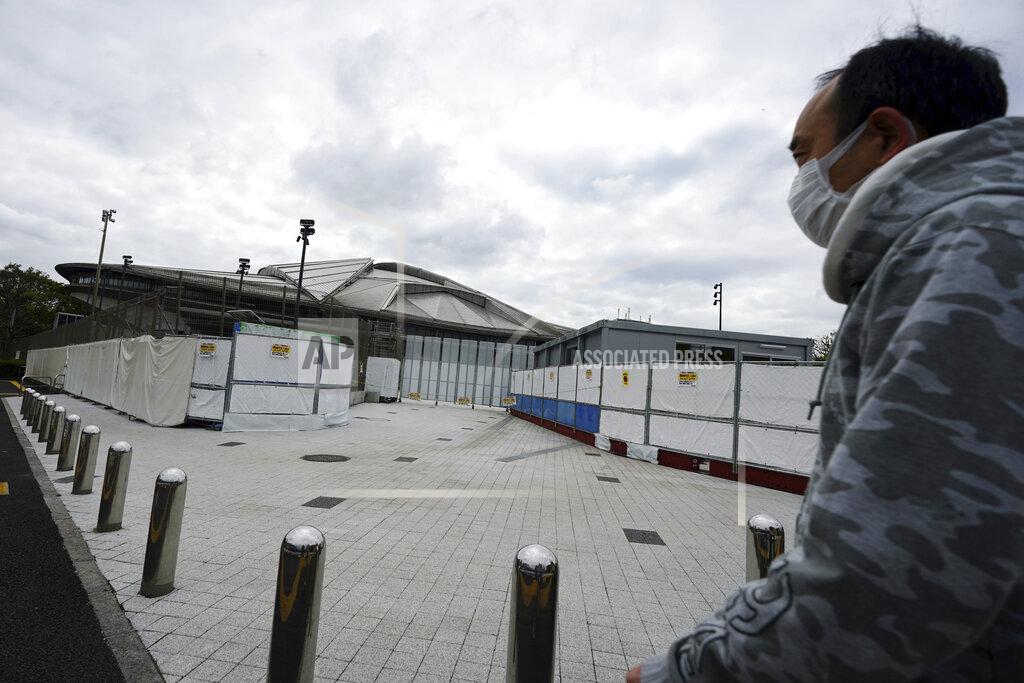 Eugene Hoshiko A man wearing a protective mask to help curb the spread of the coronavirus walks near Tokyo Metropolitan Gymnasium, one of venues for the postponed Tokyo 2020 Olympics Tuesday, April 6, 2021, in Tokyo. Many preparations are still up in the air as organizers try to figure out how to hold the postponed games in the middle of a pandemic. (AP Photo/Eugene Hoshiko)
