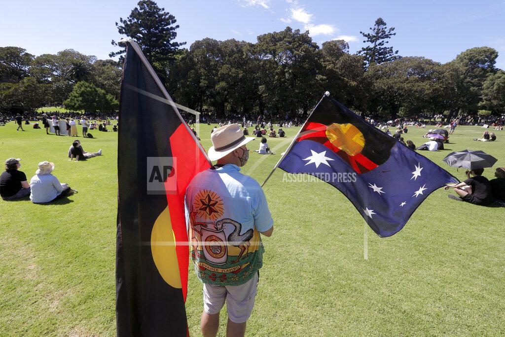 Rick Rycroft A man holds a modified Australian flag and the Aboriginal flag in a social distanced crowd during an Aboriginal-lead Invasion Day rally on Australia Day in Sydney, Tuesday, Jan. 26, 2021. Many of Australia's First Nations people say that sovereignty has never been ceded and oppose ongoing colonial violence and destruction. (AP Photo/Rick Rycroft)
