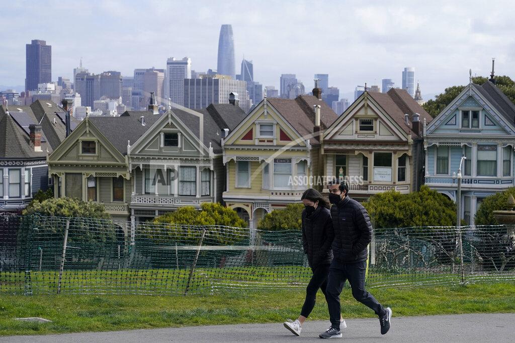 Jeff Chiu FILE - In this March 13, 2021, file photo, people wearing masks walk along at path in front of the "Painted Ladies," a row of historical Victorian homes, and the San Francisco skyline at Alamo Square Park during the coronavirus pandemic in San Francisco. California will offer six "dream vacation" incentives to spur more people to get coronavirus vaccinations, California Gov. Gavin Newsom said Monday, June 14, 2021, on the eve of the state's awarding of $15 million in cash prizes. Newsom spoke in San Francisco, site of one of the six vacation packages offered by various providers through Visit California, the state's quasi-independent travel promotion arm. (AP Photo/Jeff Chiu, File)