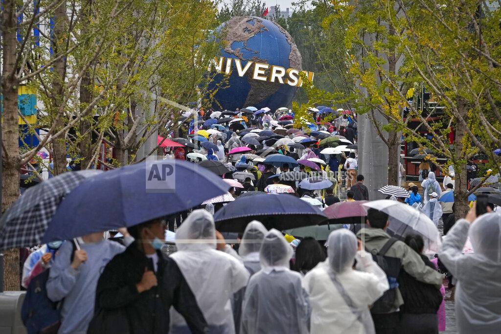 Andy Wong People wearing raincoats and carrying umbrellas walk through a plaza near the entrance of Universal Studios Beijing in Beijing, Monday, Sept. 20, 2021. Thousands of people brave the rain visit to the newest location of the global brand of theme parks which officially opens on Monday. (AP Photo/Andy Wong)