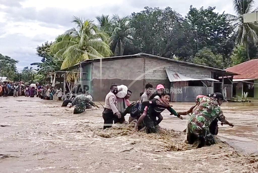 Uncredited In this image made from video, soldiers and police officers assist residents to cross a flooded road in Malaka Tengah, East Nusa Tenggara province, Indonesia, Monday, April 5, 2021. Multiple disasters caused by torrential rains in eastern Indonesia have left dozens of people dead and missing and displaced thousands, the country's disaster relief agency said Monday. (AP Photo)