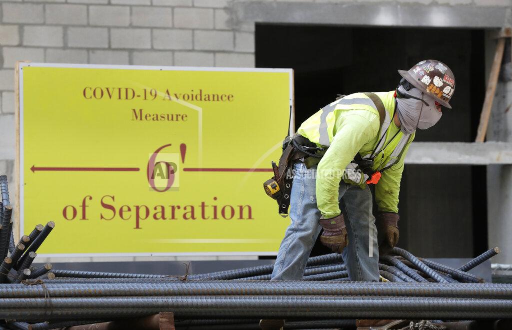 FILE - In this April 9, 2020, file photo, a construction worker wears a protective mask during the coronavirus pandemic as he unloads a truck standing in front of a sign reminding people to stay 6 feet apart, in downtown Miami. There's been a spike of new infections among construction workers in Austin, Texas, where that sector recently returned to work. (AP Photo/Wilfredo Lee, File)